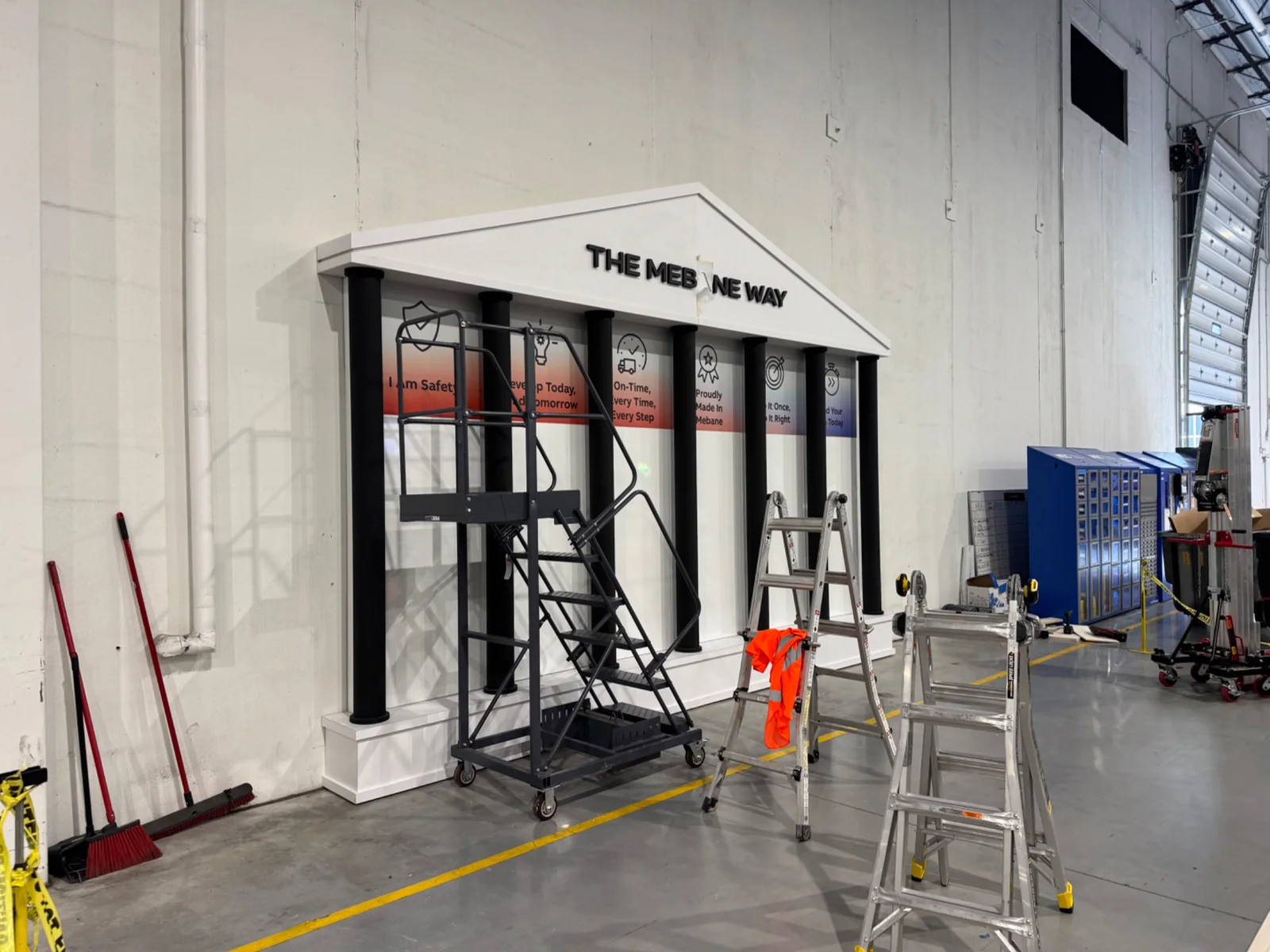 Permanent branded display installation in progress with ladders, lift equipment, and finish work underway